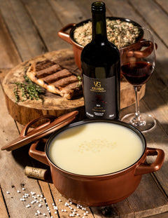 Crock of white sauce with a bottle of red wine and a glass on a wooden table.