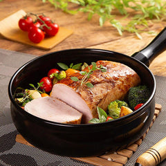 Sliced roasted meat with vegetables in a black skillet on a wooden surface.